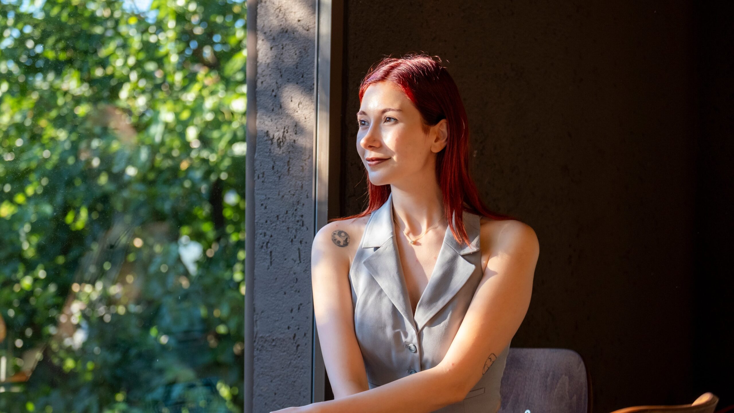 A young redhead businesswoman, dressed in office attire, smiling as she watches outside through the window